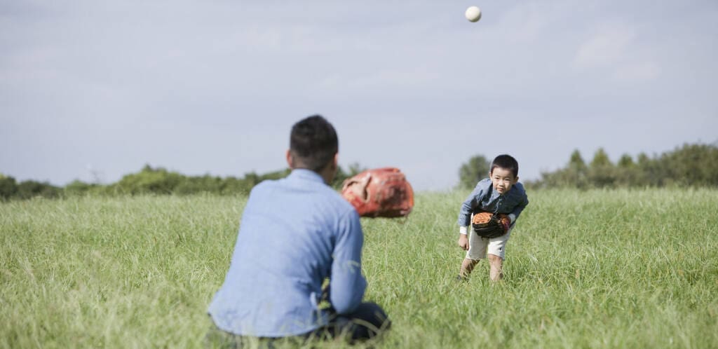 Fatherchildcatchball2024 | my stellaマイステラブログ|子どもの好きが育つヒントと親子の時間 夕暮れ時の公園や庭で、父親と子どもがキャッチボールをする様子。 柔らかな夕日の光が差し込み、両者の表情が優しく照らされている。 父親は仕事帰りを思わせるビジネスカジュアル(Yシャツの袖をまくり、ネクタイを緩めた状態)。 子どもは真剣な表情でボールをキャッチしようとしている瞬間。