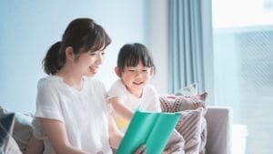 明るいリビングで、母親が娘と一緒に絵本を楽しそうに読み聞かせしている様子。