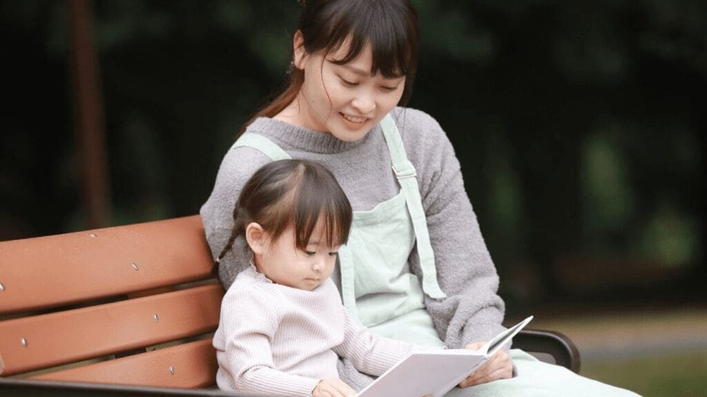 公園のベンチで読み聞かせを楽しむ母と娘|my stella | my stellaマイステラブログ|子どもの好きが育つヒントと親子の時間 公園のベンチで母親が幼い女の子に絵本を読み聞かせている様子。親子の穏やかなひととき。