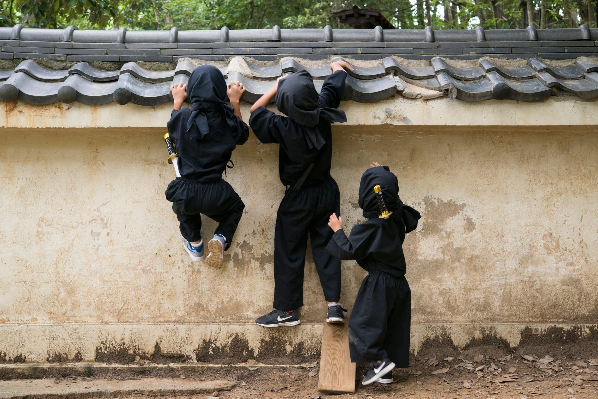 忍者衣装を着た子どもたちが、修行の一環として塀をよじ登る様子