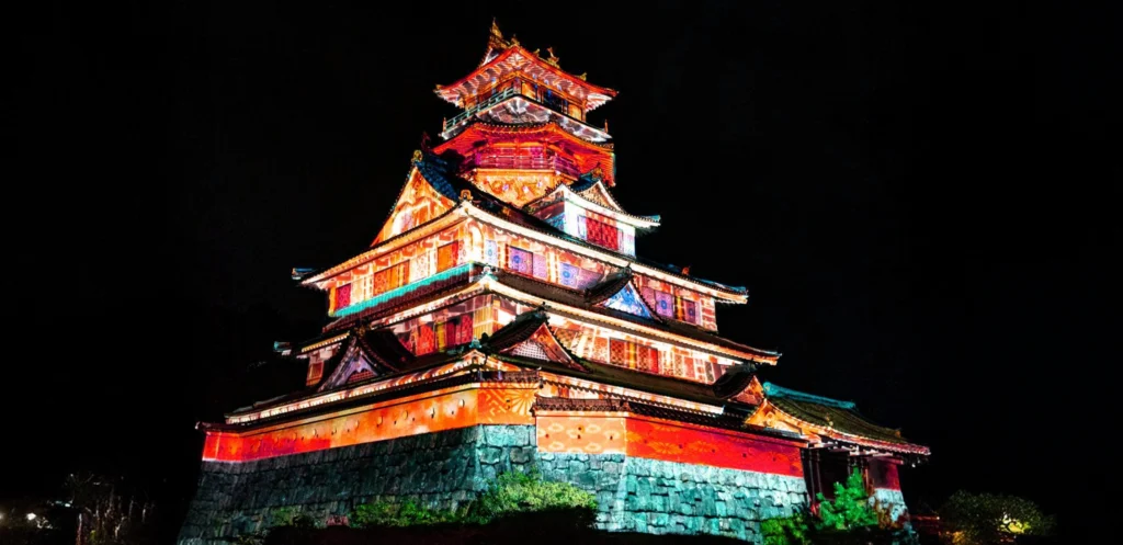 Ise-ninja-kingdom-night-projection-mapping 三重県伊勢市のともいきの国 伊勢忍者キングダムの城郭を夜間にライトアップし、カラフルなプロジェクションマッピングを映し出している様子